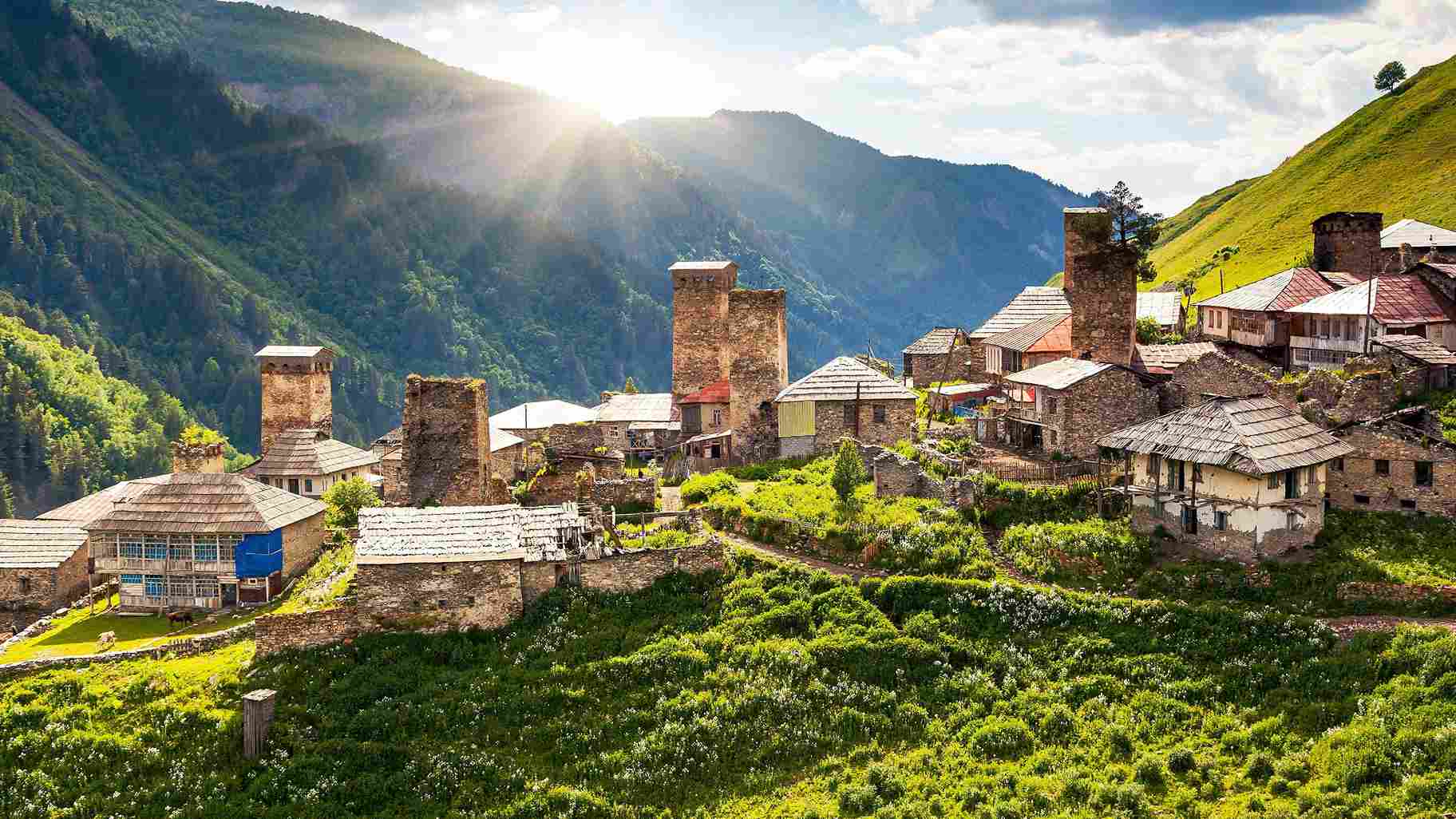 نمایی از روستای کوهستانی اوشگولی در منطقه سوانتی گرجستان، با برج‌های دفاعی سنگی قرون وسطایی، خانه‌های سنتی و نور خورشید بر دامنه‌های سرسبز قفقاز