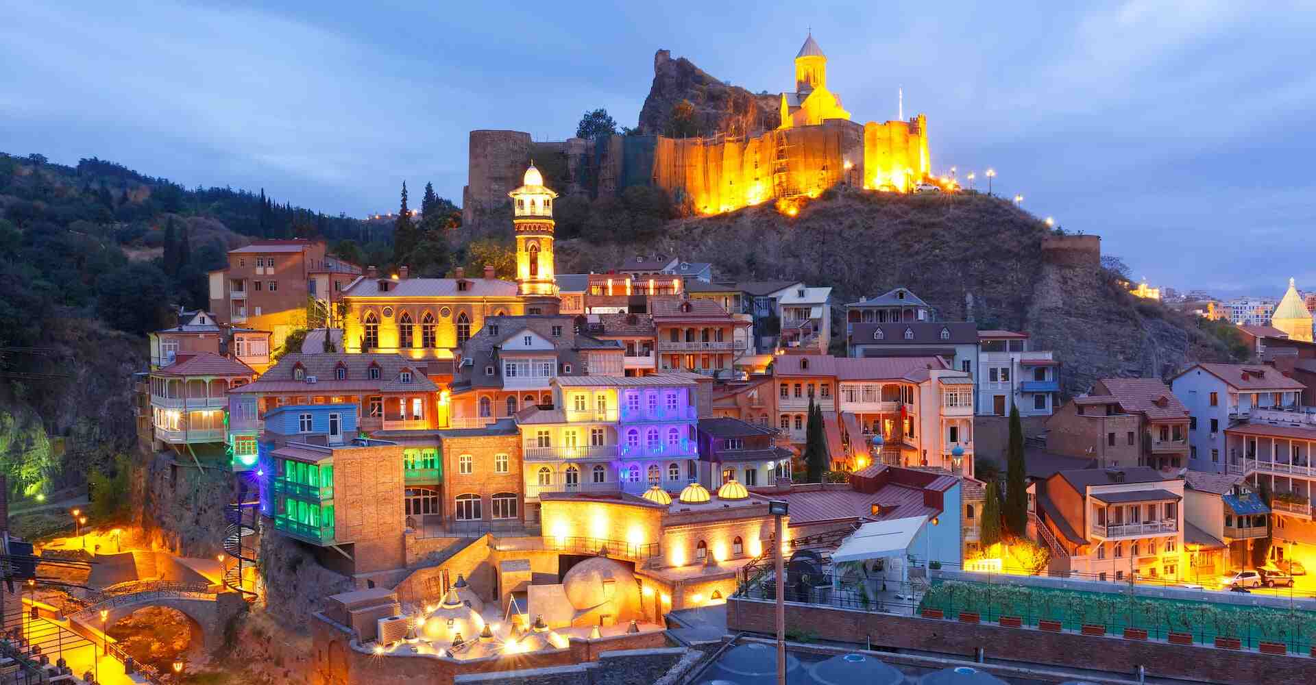 نمای شبانه از محله تاریخی آبانتوبانی در تفلیس، پایتخت گرجستان، با معماری رنگارنگ سنتی و قلعه ناریکالا روشن در پس‌زمینه
