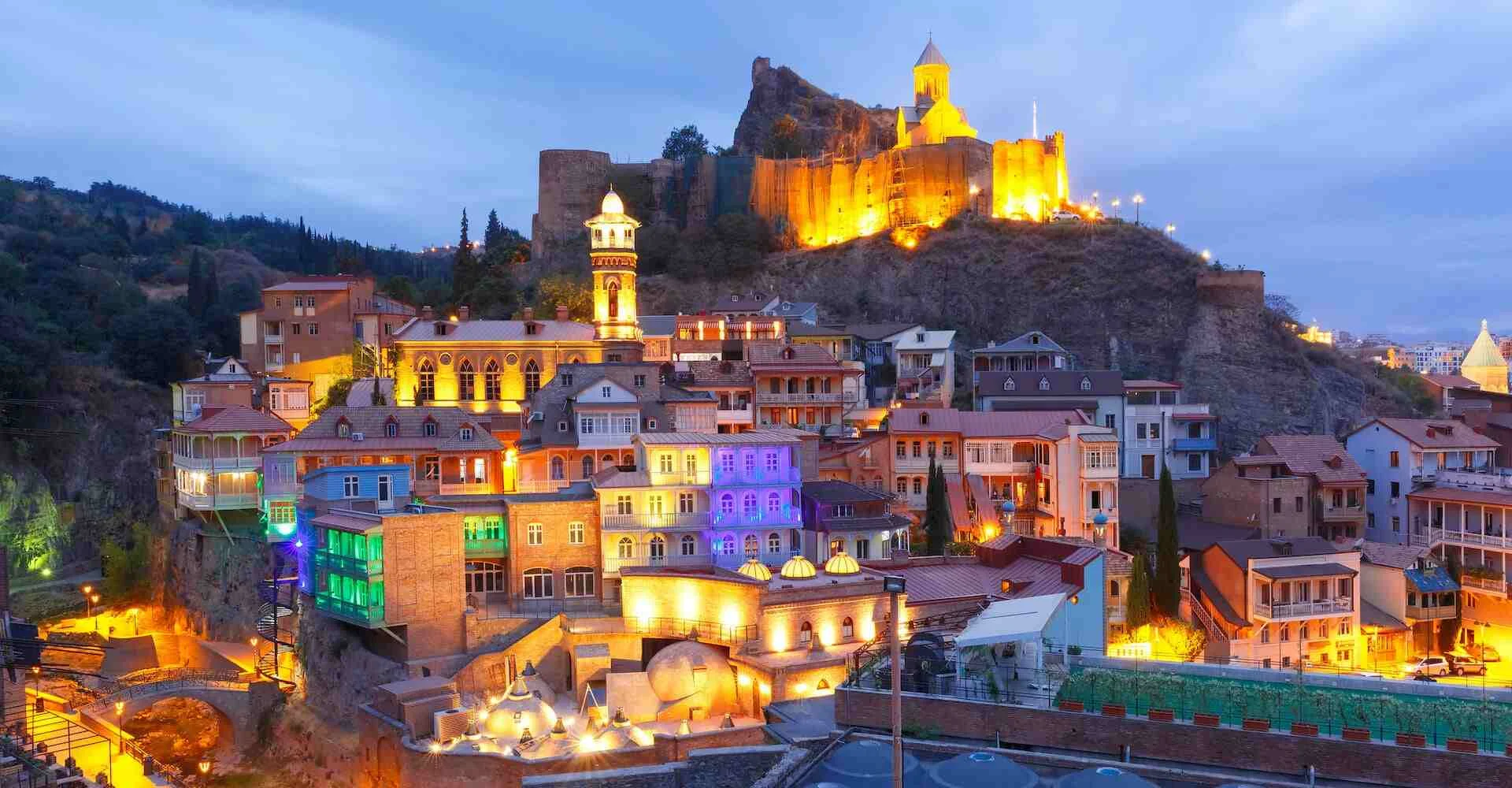 گردشگری | مهاجرت نمای شبانه از محله تاریخی آبانتوبانی در تفلیس، پایتخت گرجستان، با معماری رنگارنگ سنتی و قلعه ناریکالا روشن در پسزمینه